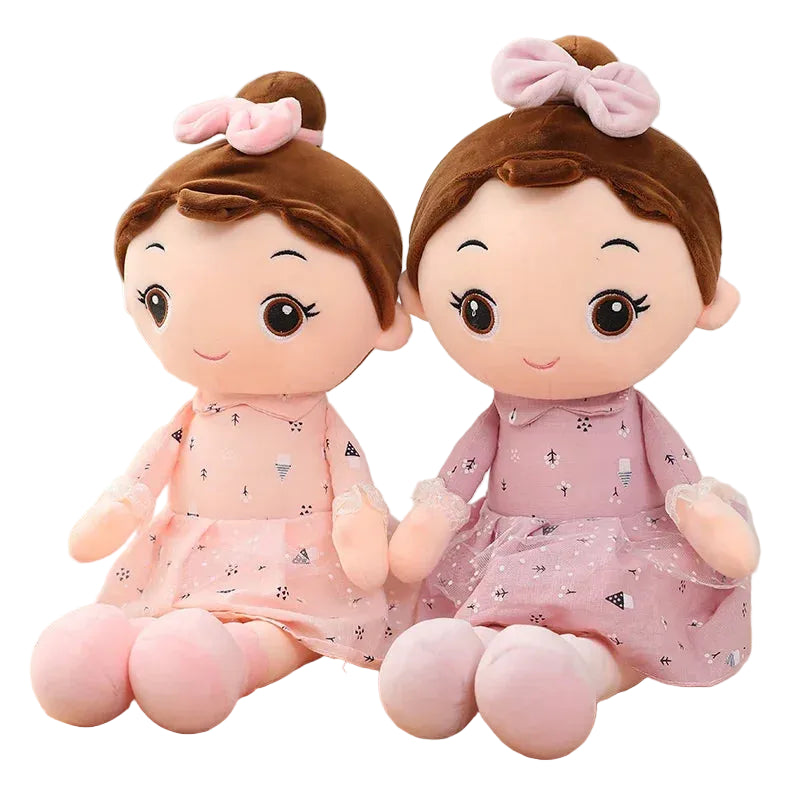 Two plush toys with brown hair and pink dresses on a wooden surface.